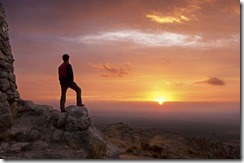 Man on top of a mountain standing contemplates the dawn